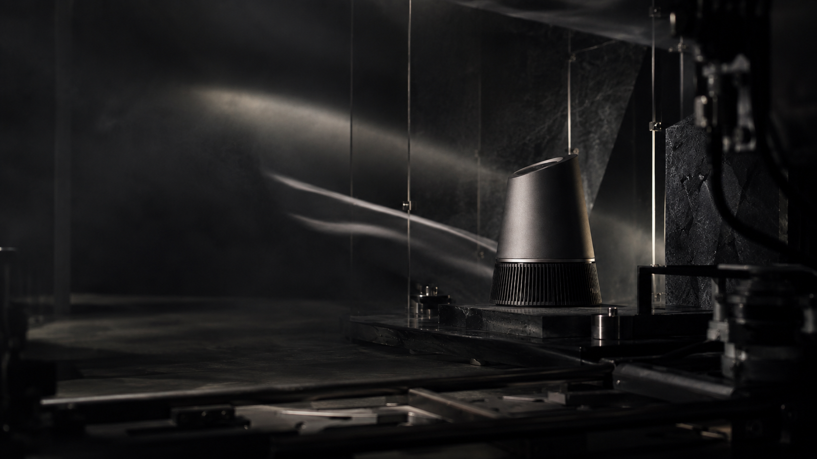 Behind-the-scenes precision product set showing motion elements, haze, reflections, and camera equipment around a static hero object.